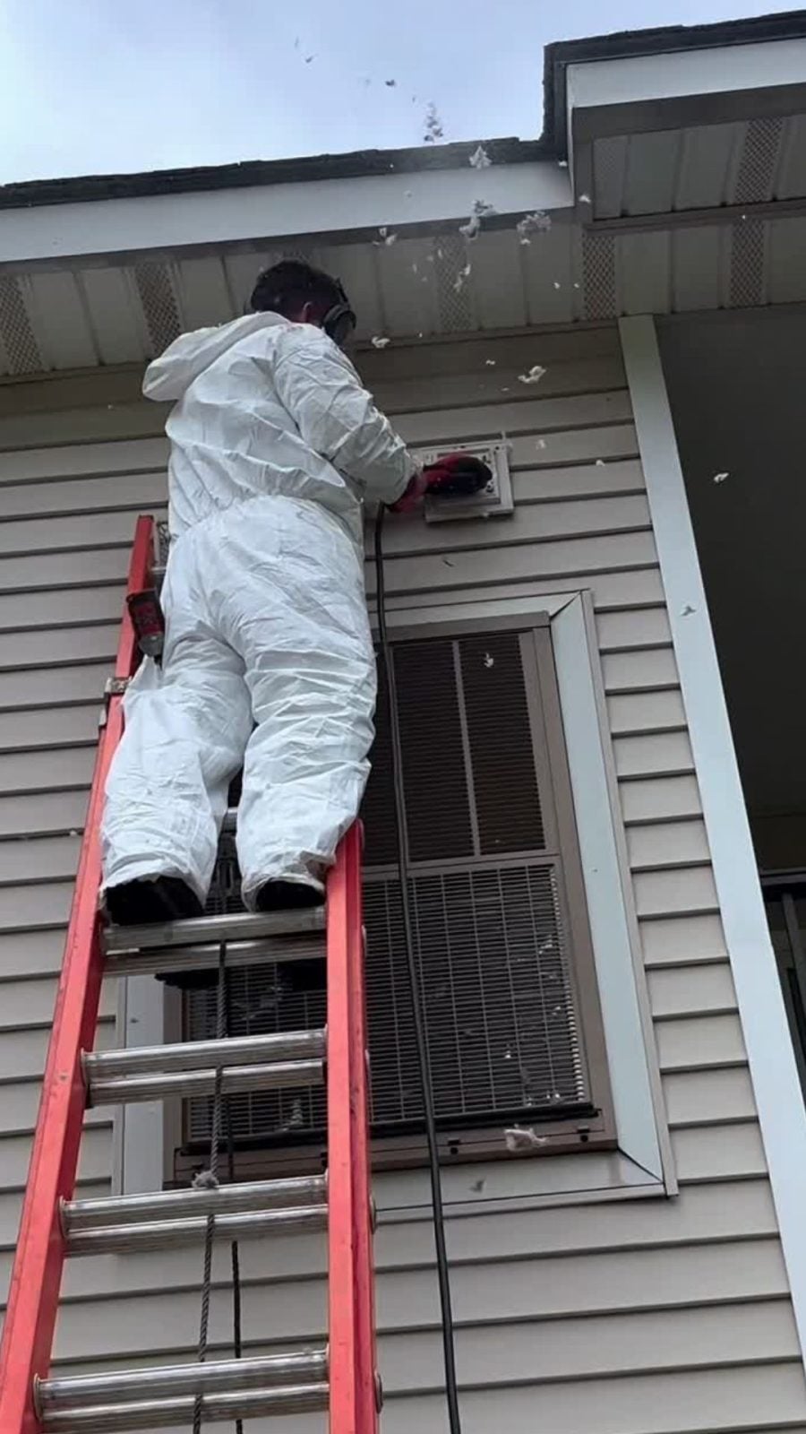 PCRS technician on a ladder cleaning an exterior dryer vent hood, debris visibly clearing