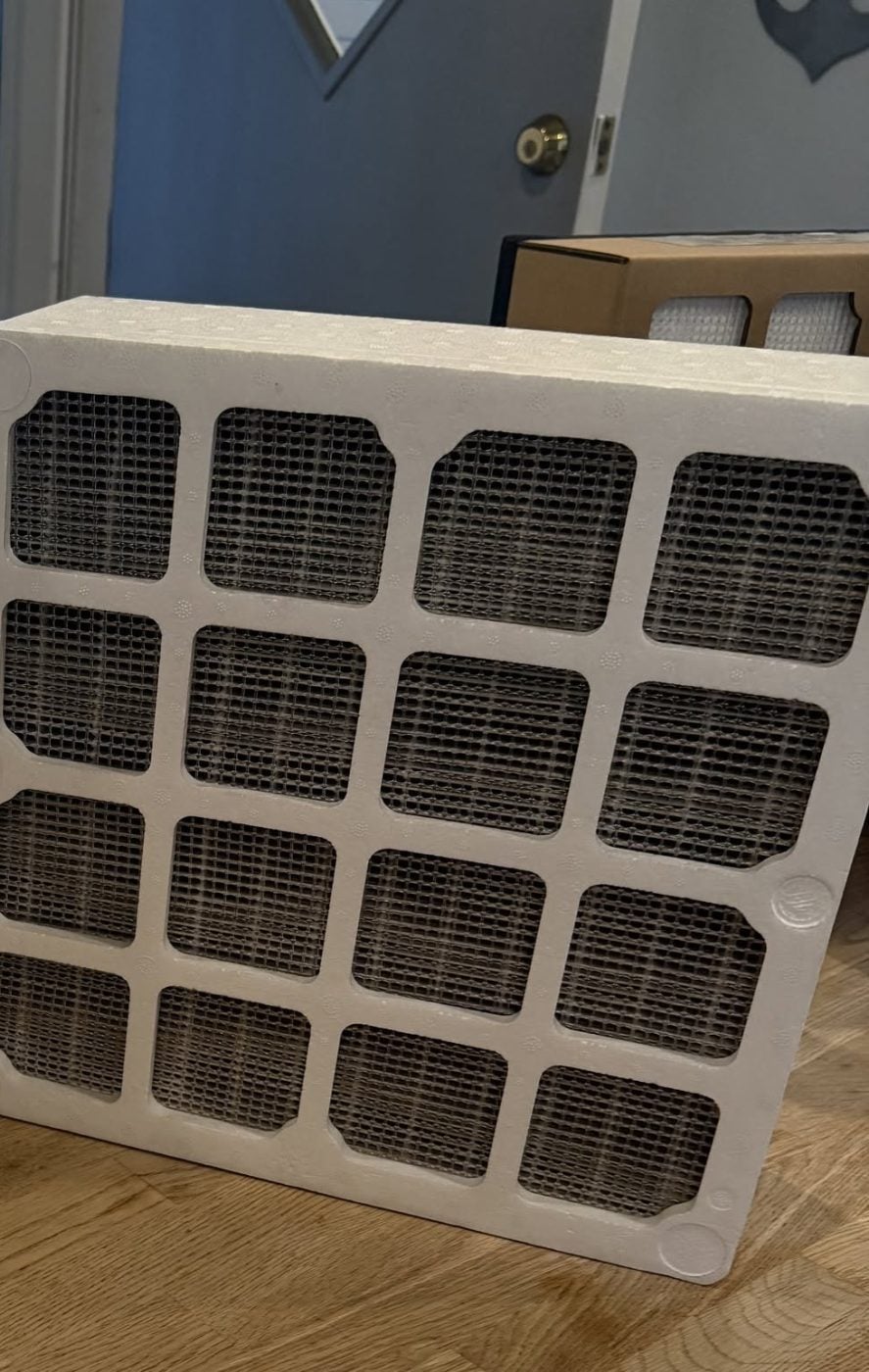 A heavily soiled residential HVAC filter, its media dark with trapped dust and debris