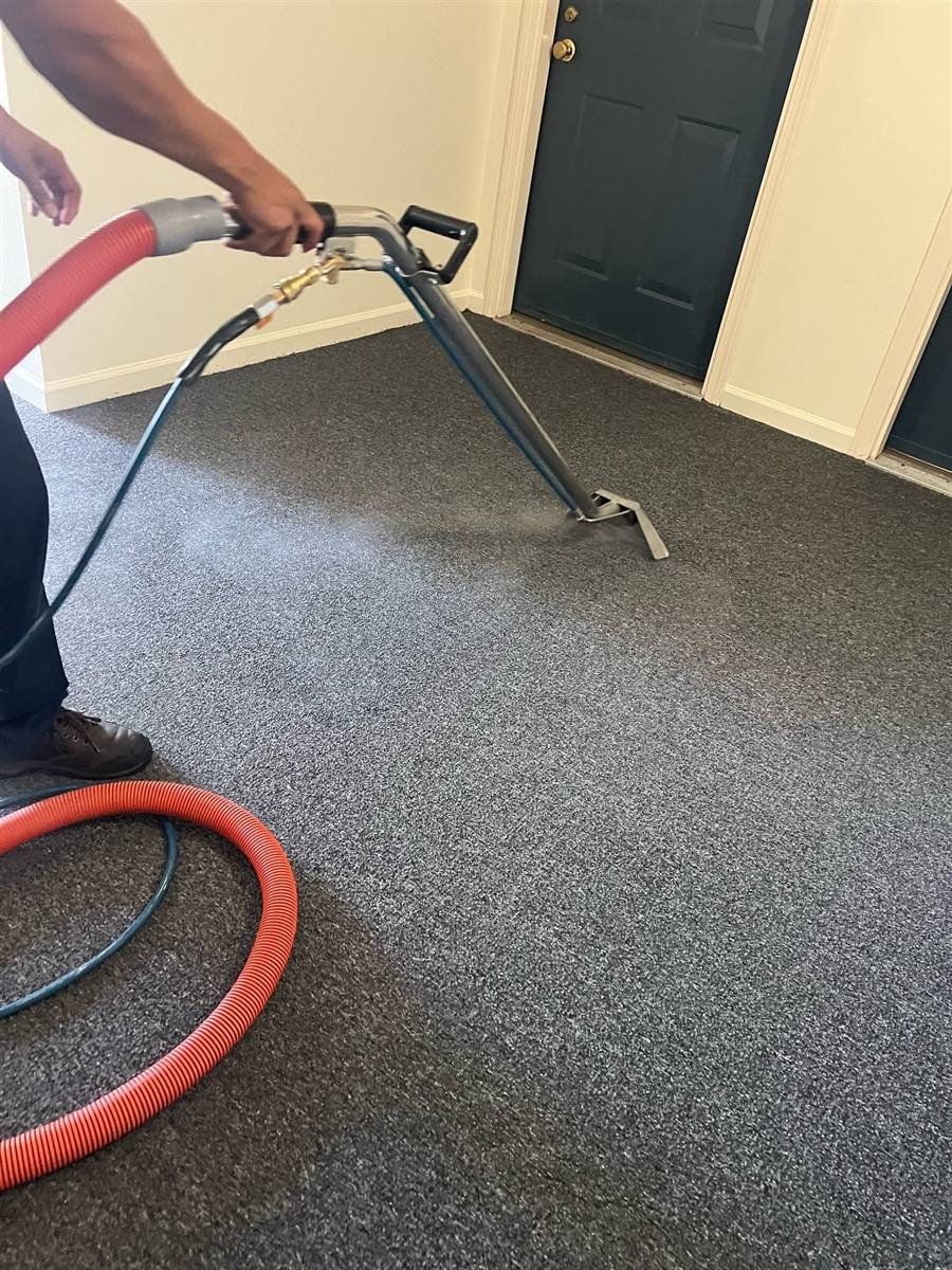 Technician steam cleaning commercial carpet with a truck-mount wand