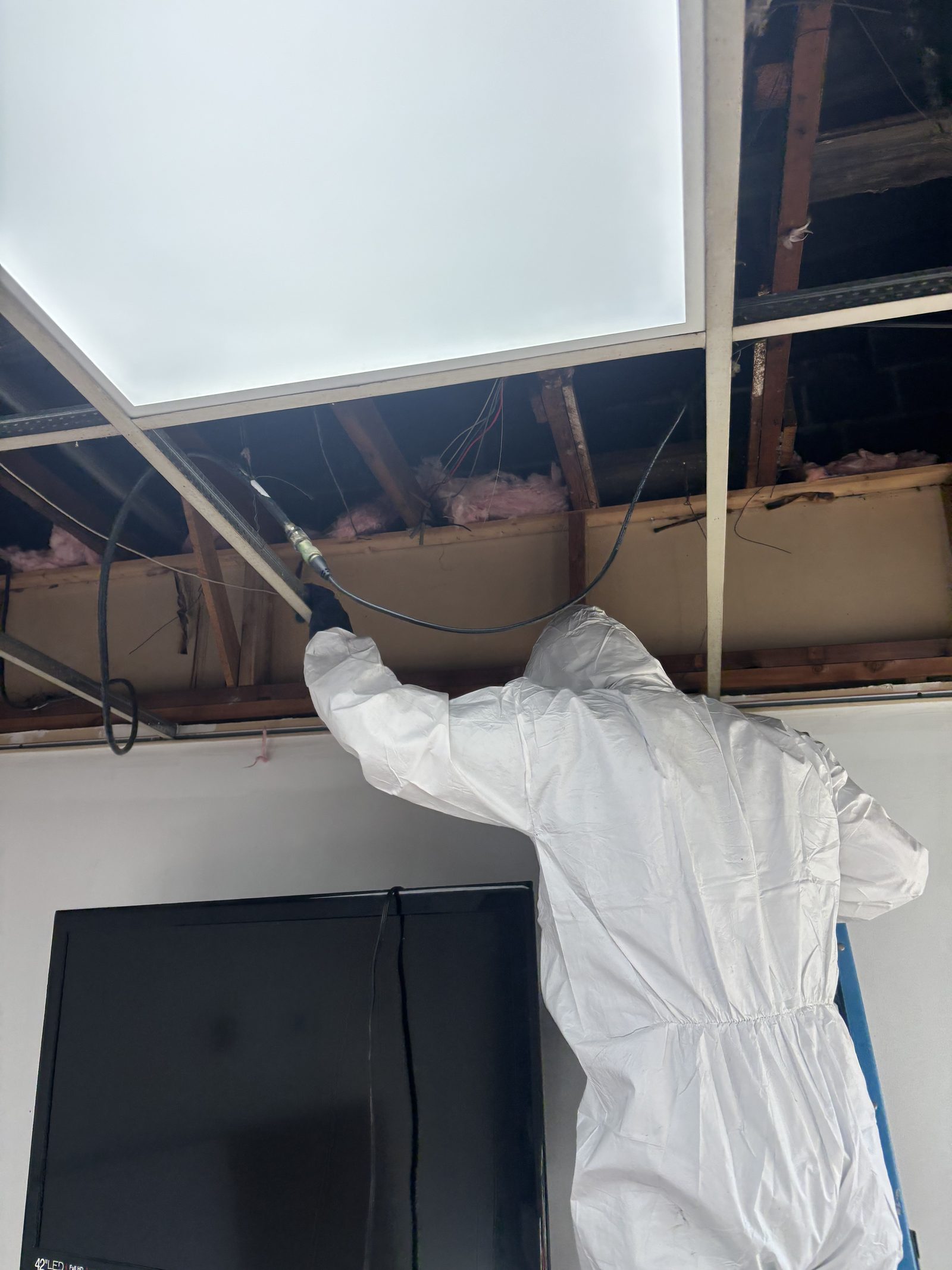 A PCRS technician in a Tyvek suit HEPA-vacuuming a ceiling