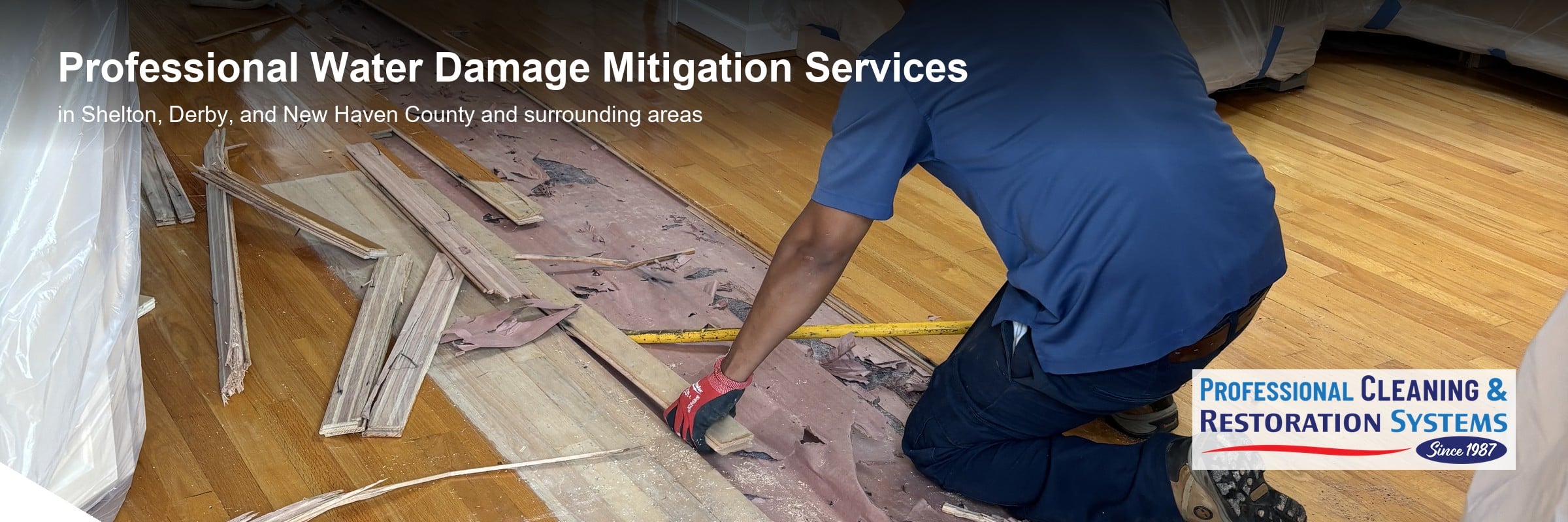 pcrs-water-damage-mitigation-banner Water damage mitigation in Shelton CT — PCRS technicians lifting water-damaged hardwood flooring off the subfloor in a room sheeted in plastic